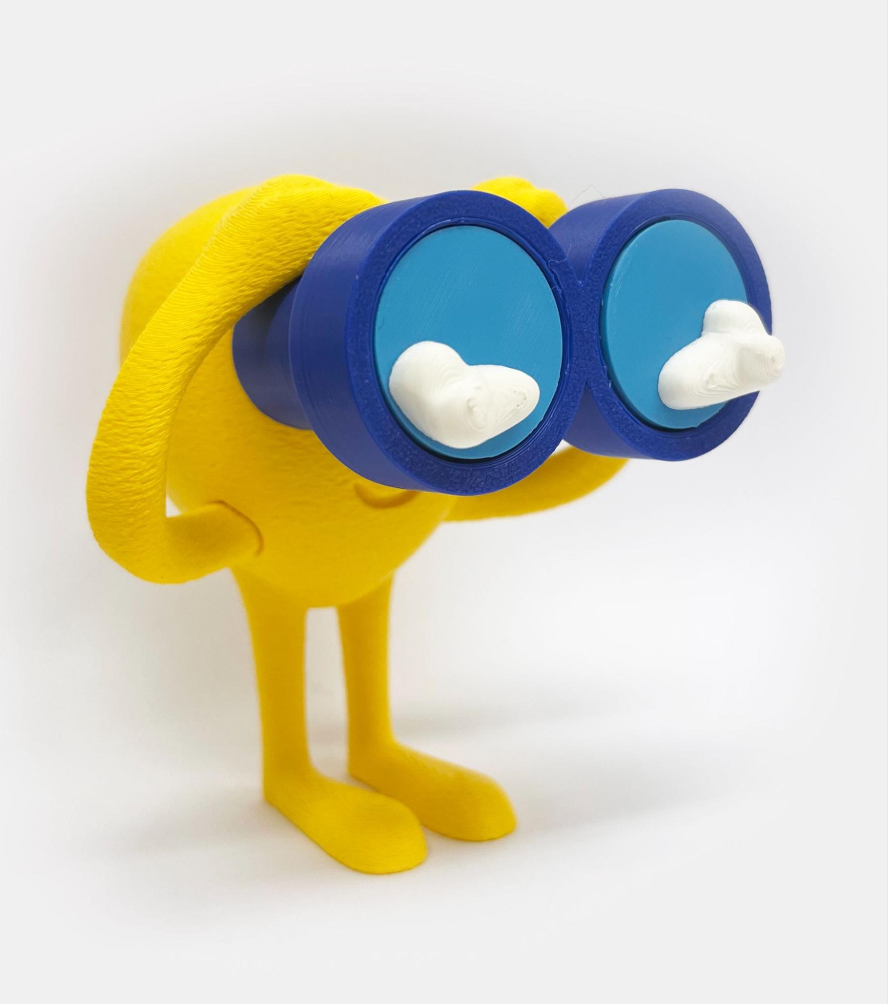 Audiodescrição: fotografia vertical do mascote tridimensional. Ele tem a cabeça junto com o corpo em forma oval amarela, mãos e pés grandes e um breve sorriso. Segura um grande binóculo azul escuro, com lentes azuis claras de onde projetam duas nuvens brancas. Fim da audiodescrição.<br />
